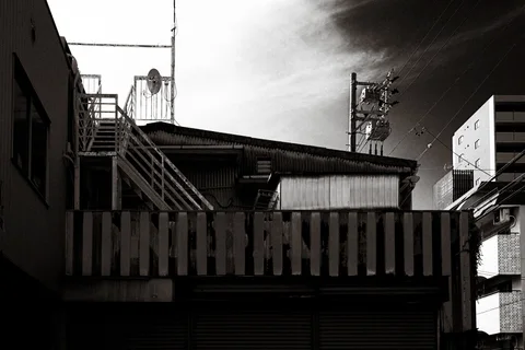 Exterior metal stairs rise above a weathered building beneath dark clouds in a black and white view.