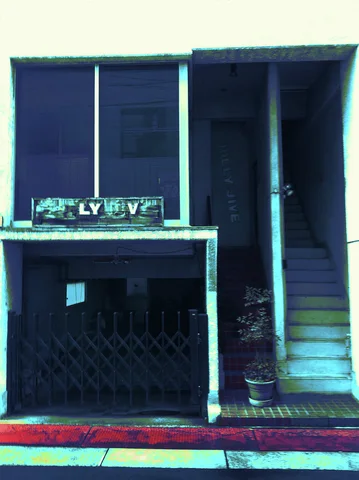 A narrow dark storefront stands beside an enclosed staircase beneath pale upper walls.