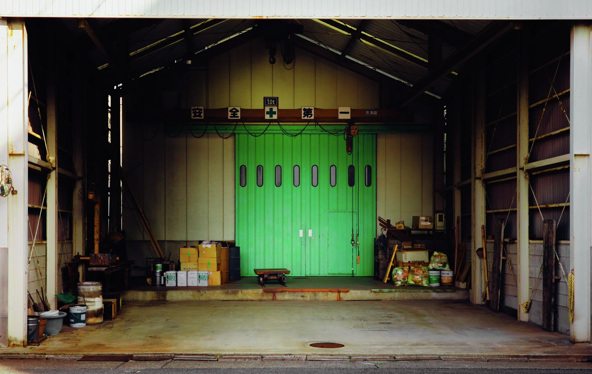 An open industrial bay leads to bright green doors with narrow oval windows and scattered containers.