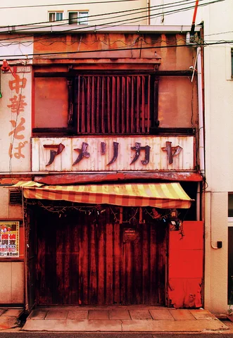 A weathered red storefront has a striped awning and faded sign below a barred upper window.