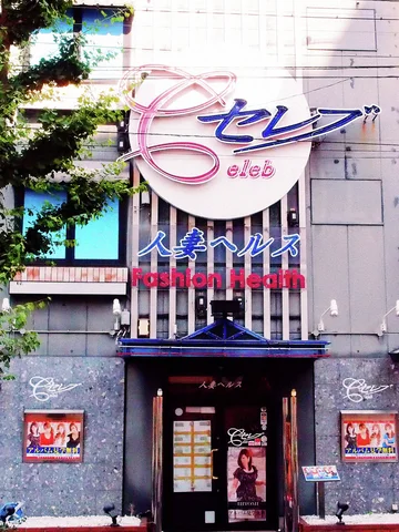 A tall gray storefront displays a large pink-and-blue sign above a dark entrance and colorful posters.
