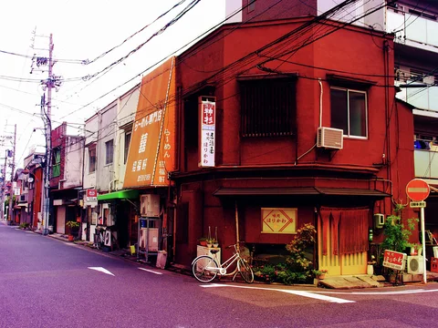 A red corner building overlooks a quiet street with a bicycle beside its shaded ground-floor entrance.