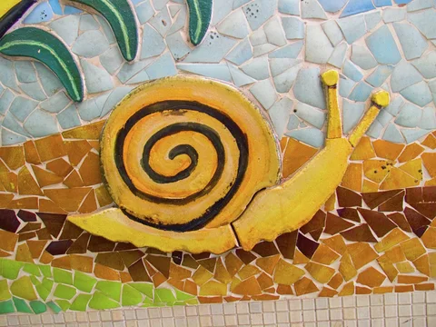 A yellow snail with a dark spiral shell stretches across a mosaic of blue, brown, and green tiles.