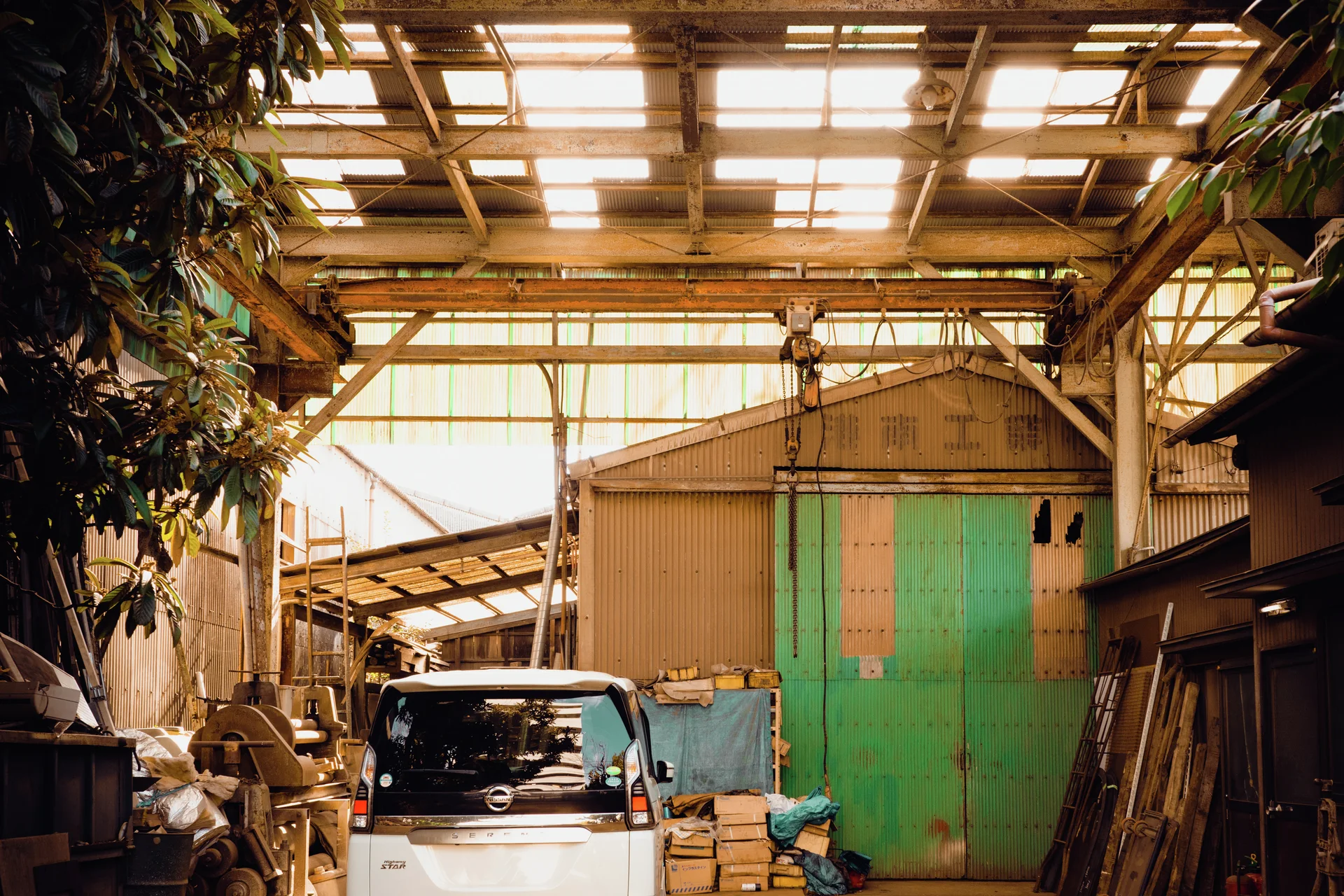 A small white vehicle stands beneath a translucent shed roof beside tall green doors and equipment.