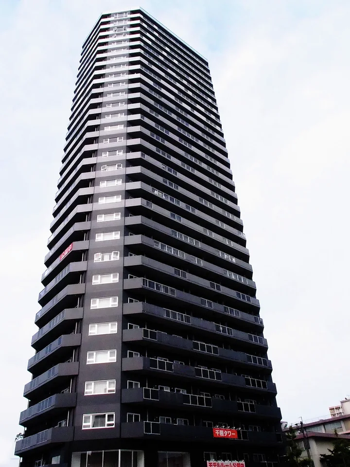 A tall dark tower has closely stacked horizontal balconies and a tapered silhouette against pale sky.