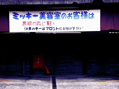 A broad white sign with blue lettering spans a dark parking entrance above a red box and cone.
