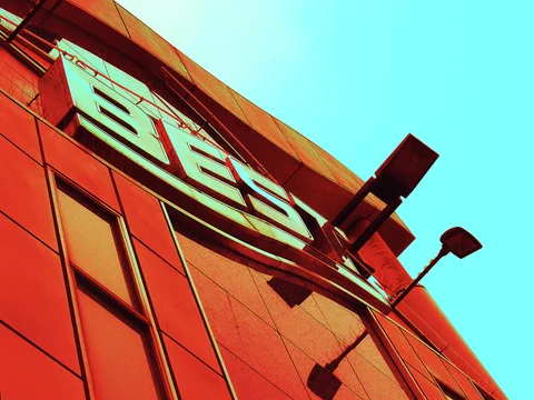 Large pale lettering and two projecting lamps stand against a vivid orange building and turquoise sky.