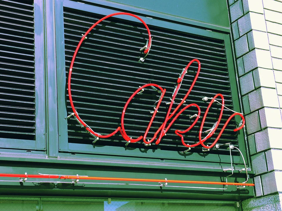 Red cursive neon tubing spells Cake across a green louvered window above horizontal neon bands.