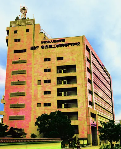 A tall tan building with rows of narrow windows has a small sculptural figure on its rooftop.