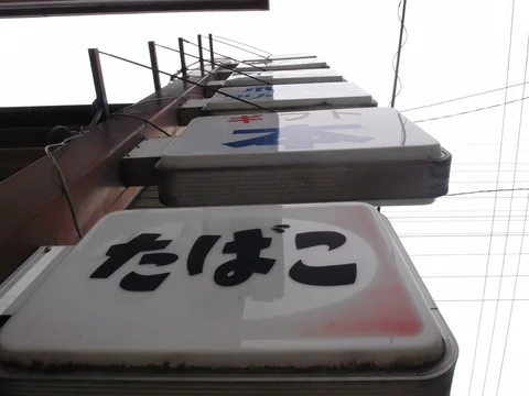 Projecting pale business signs climb a building viewed from below beneath a mesh of overhead wires.