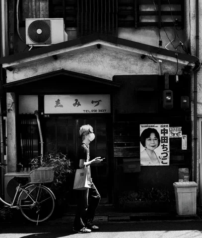 A person stands beside a bicycle outside a dark storefront with a portrait poster in black and white.