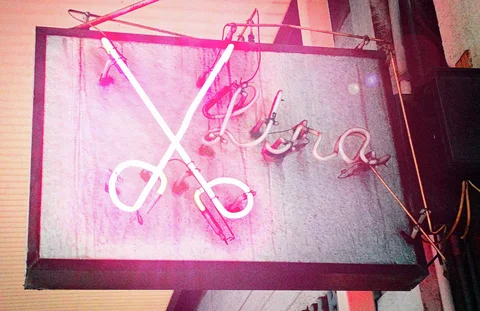 Pink neon scissors and cursive lettering overlap on a hanging rectangular salon sign.