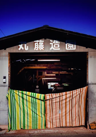 Green-yellow and pink striped fabric closes the lower opening of a dark wooden workshop entrance.
