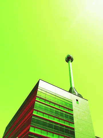 A slender rooftop tower with a circular cage-like top rises above a building beneath a vivid green sky.