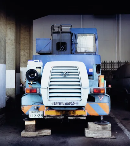 A blue industrial vehicle with a broad white grille stands on blocks beneath a dark overhang.