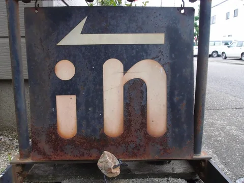 A pale left-pointing arrow and lowercase in lettering mark a rusted dark metal sign.