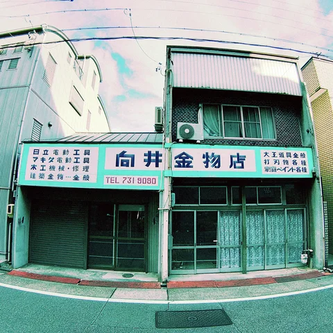 A long Japanese shop sign spans a narrow two-story building above closed shutters and curtained windows.