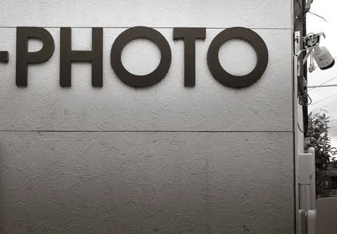Large dark PHOTO letters project from a lightly textured exterior wall in black and white.