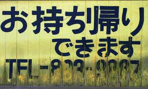 Bold dark characters and a faded telephone number fill a stained yellow rectangular sign.