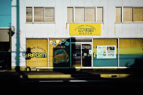 Yellow and turquoise storefront panels surround glass doors beneath upper windows and a yellow sign.