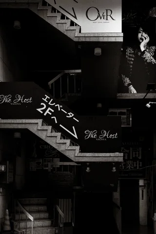 White zigzag stair edges and business signs punctuate a dark building facade in black and white.