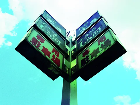 Stacked rectangular business signs project symmetrically from a central pole against turquoise sky and pale clouds.