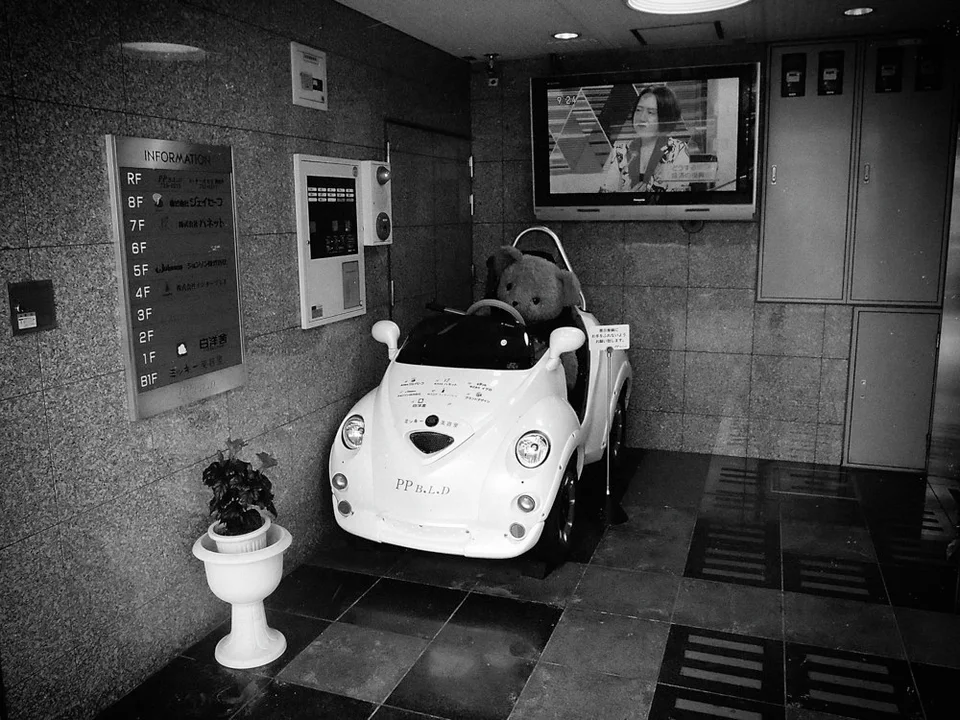 A white amusement car sits in a tiled lobby beside wall panels and a potted plant in black and white.