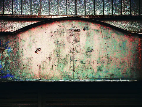 A blank arched signboard shows peeling pastel paint beneath barred textured windows.