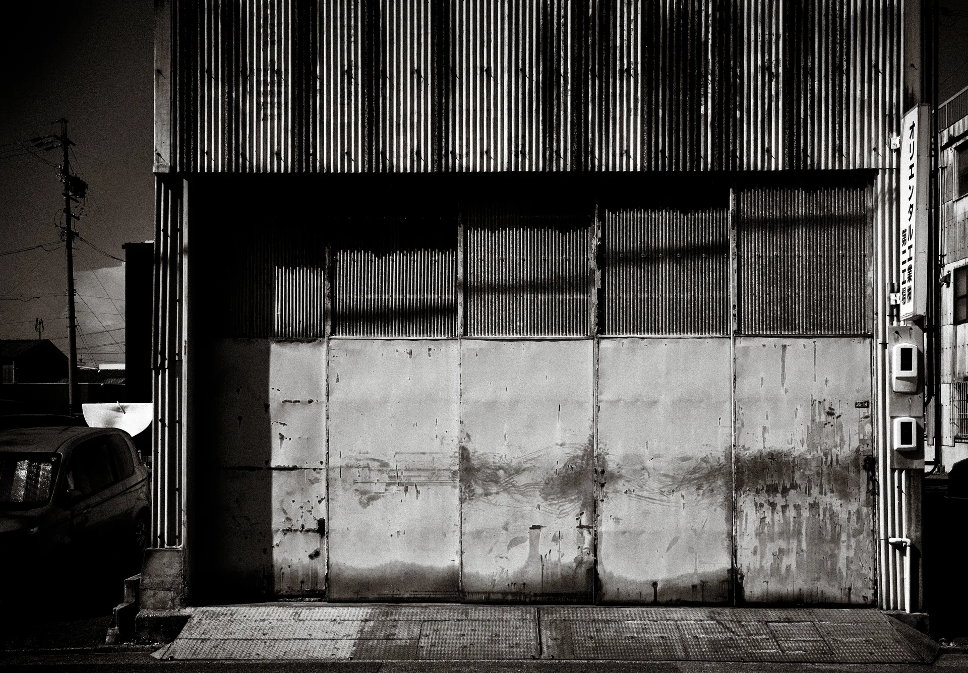 Stained pale panels close a broad opening beneath corrugated siding in black and white.