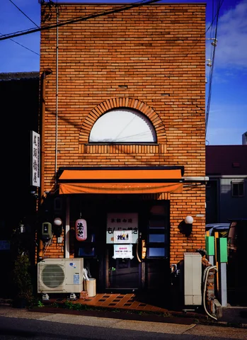A narrow brick storefront has a semicircular upper window and orange awning above a dark entrance.