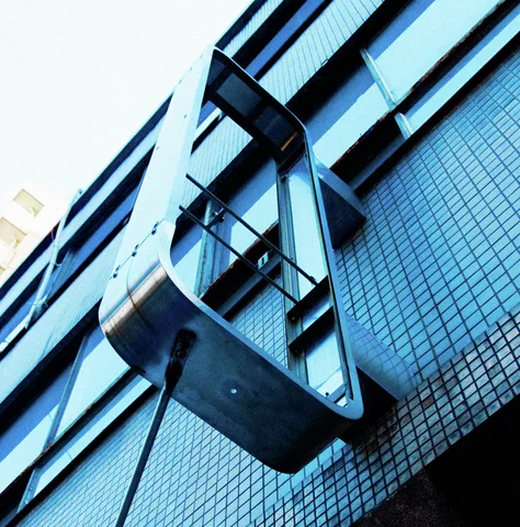 A large angular metal framework projects from a blue tiled facade beneath rows of dark windows.