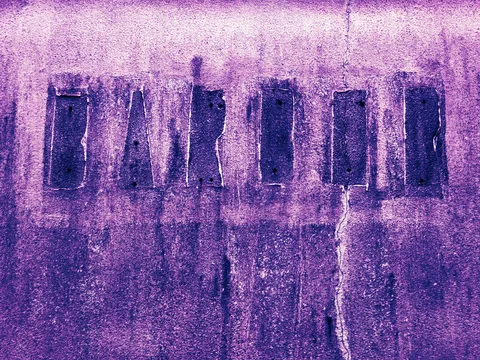 Faded dark lettering crosses a cracked, rough purple-toned wall streaked with vertical stains.