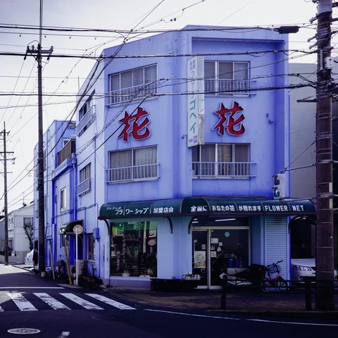Large red characters decorate a pale corner building above green shop awnings and a crosswalk.