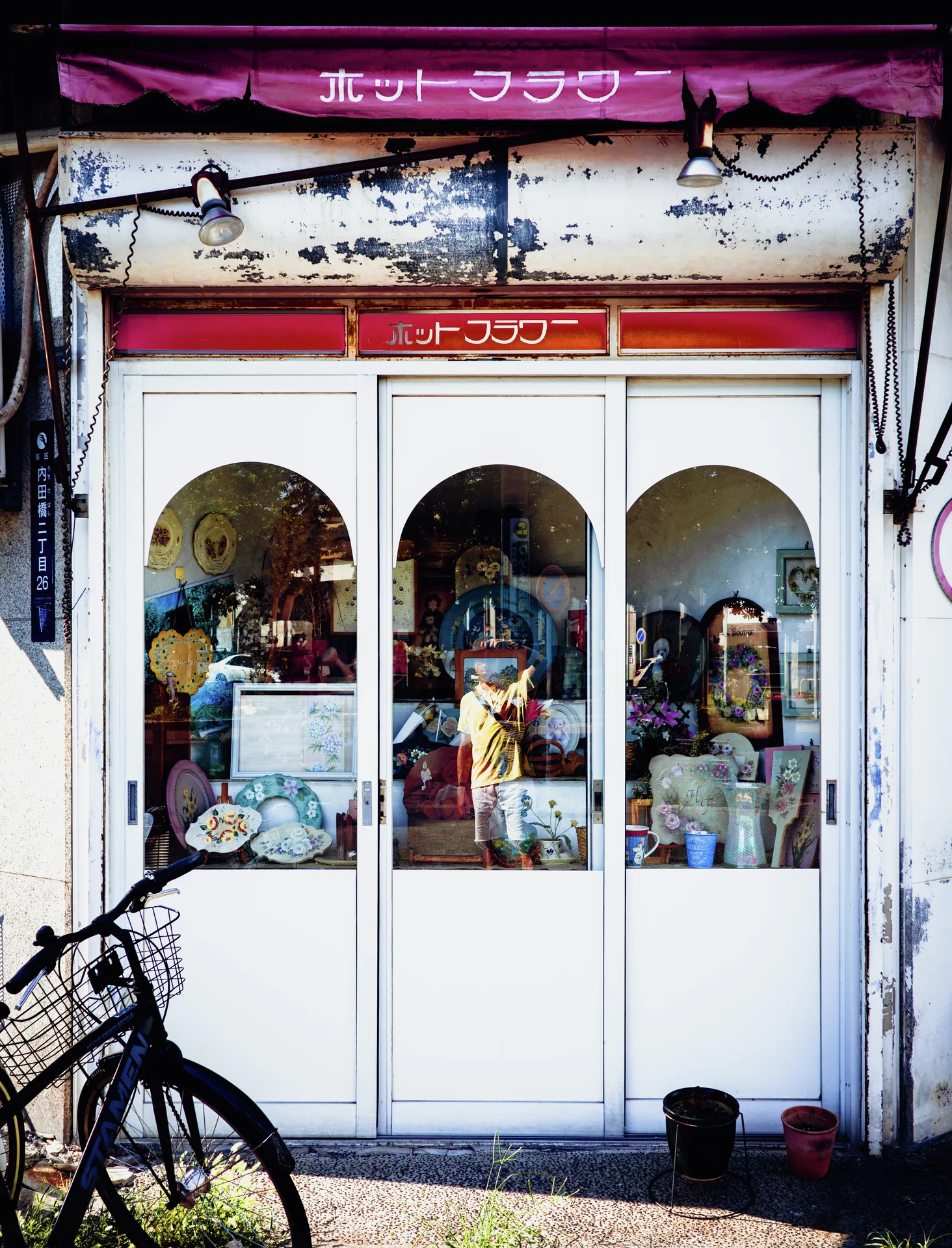 Three white arched window panels display small objects beneath a peeling sign and magenta awning.