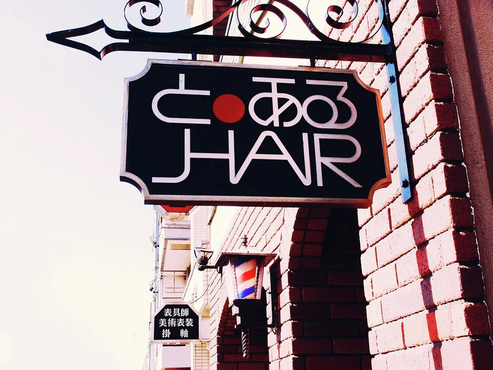 A black projecting hair-salon sign hangs from an ornate curled metal bracket beside a red brick wall.