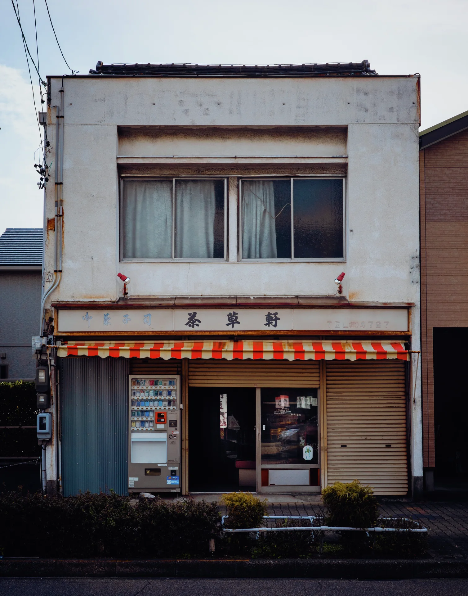 A narrow white storefront has a red and green striped awning above its entrance.