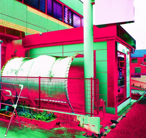 A large horizontal metal tank stands behind fencing beside a small green-and-red building.