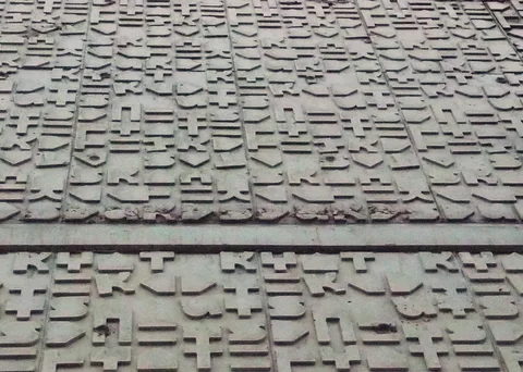 Repeated raised abstract symbols cover pale wall panels separated by narrow vertical grooves.