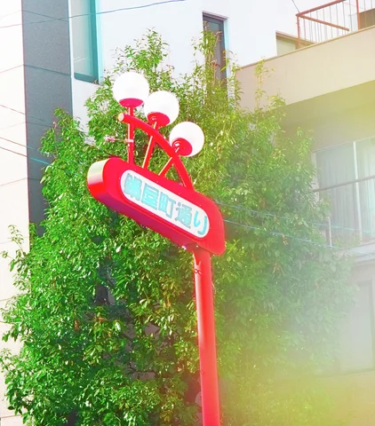 A red freestanding sign topped with three white globes stands before leafy green trees.