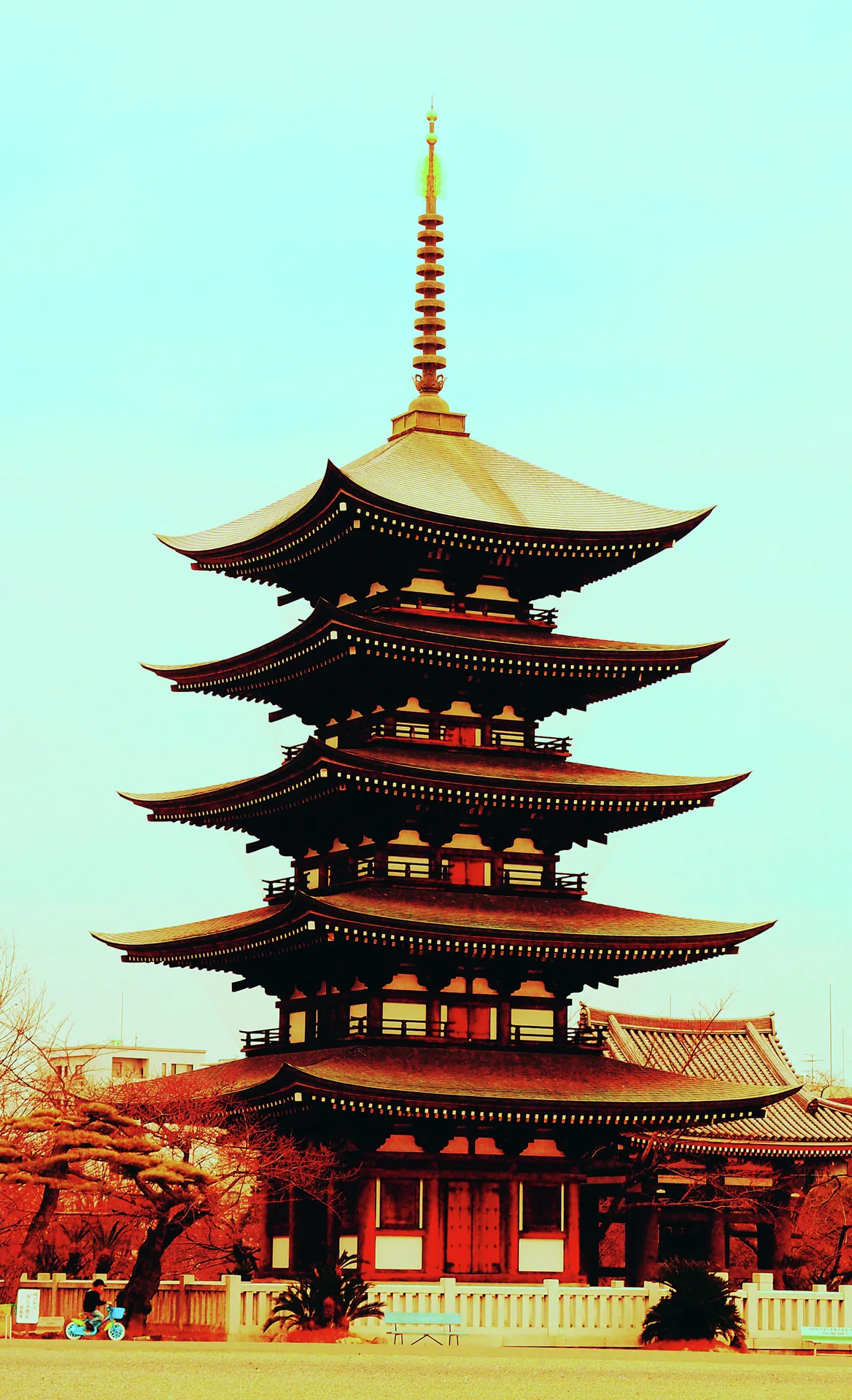 A five-tiered pagoda with curved roof corners and a tall spire rises beneath pale turquoise sky.