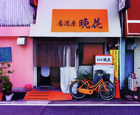 An orange bicycle stands beside a curtained restaurant entrance beneath an orange rectangular sign.