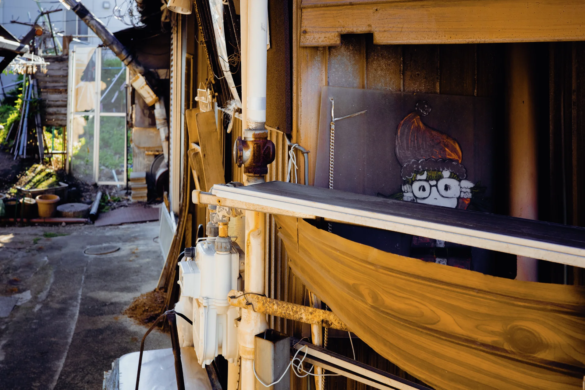 A yellow fabric hammock stretches beside a wooden house with a small illustrated owl panel and narrow garden passage.
