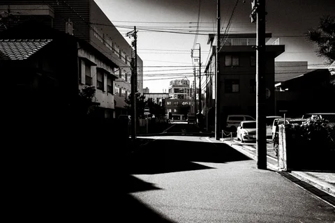 Strong angular shadows cross a quiet residential street beneath utility wires in black and white.