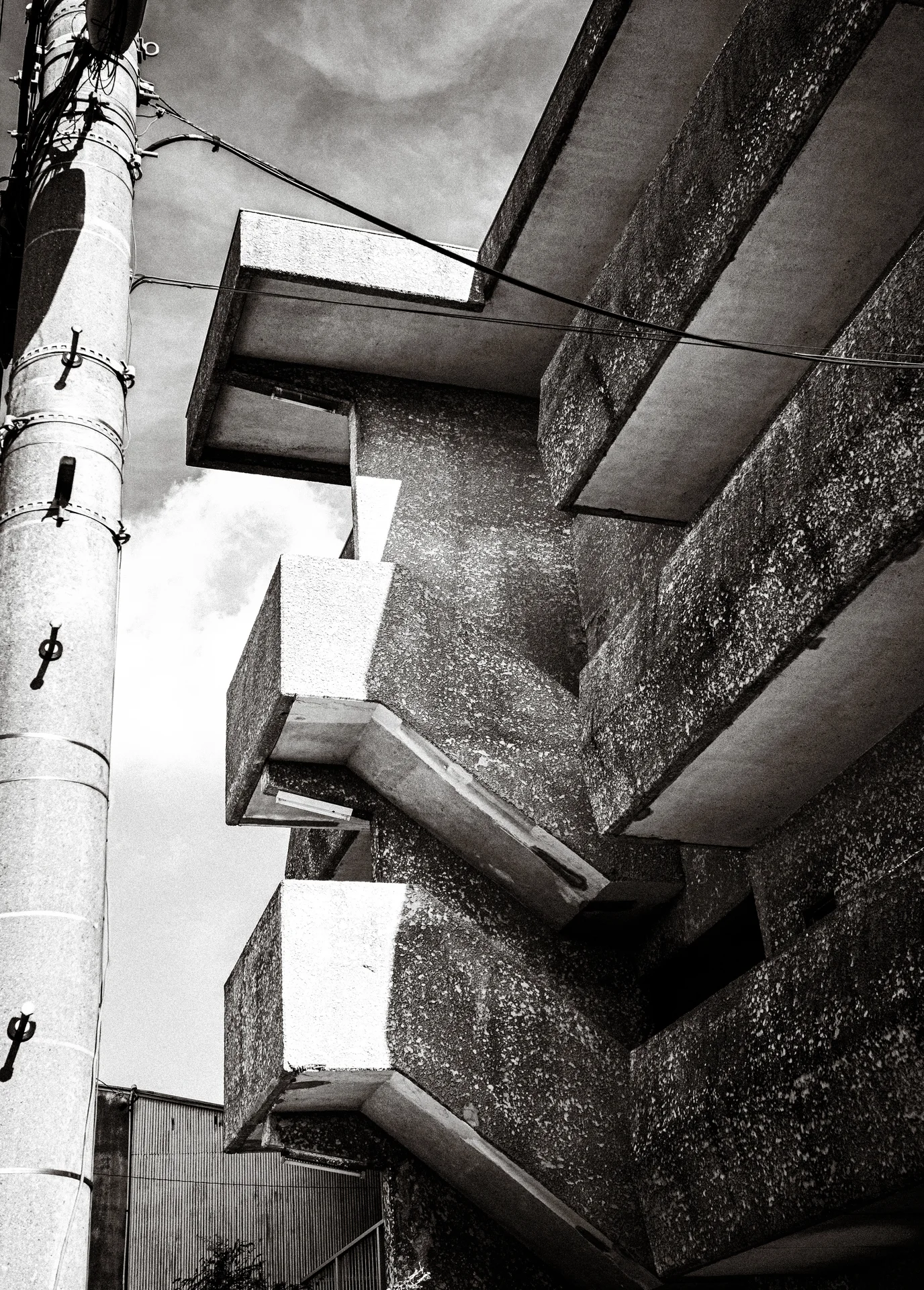 Heavy concrete ledges project from a rough wall beside a utility pole in black and white.