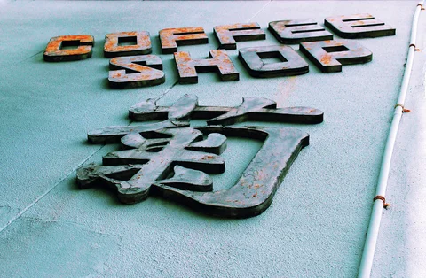 Weathered raised coffee shop lettering and a large Japanese character project from a pale blue wall.