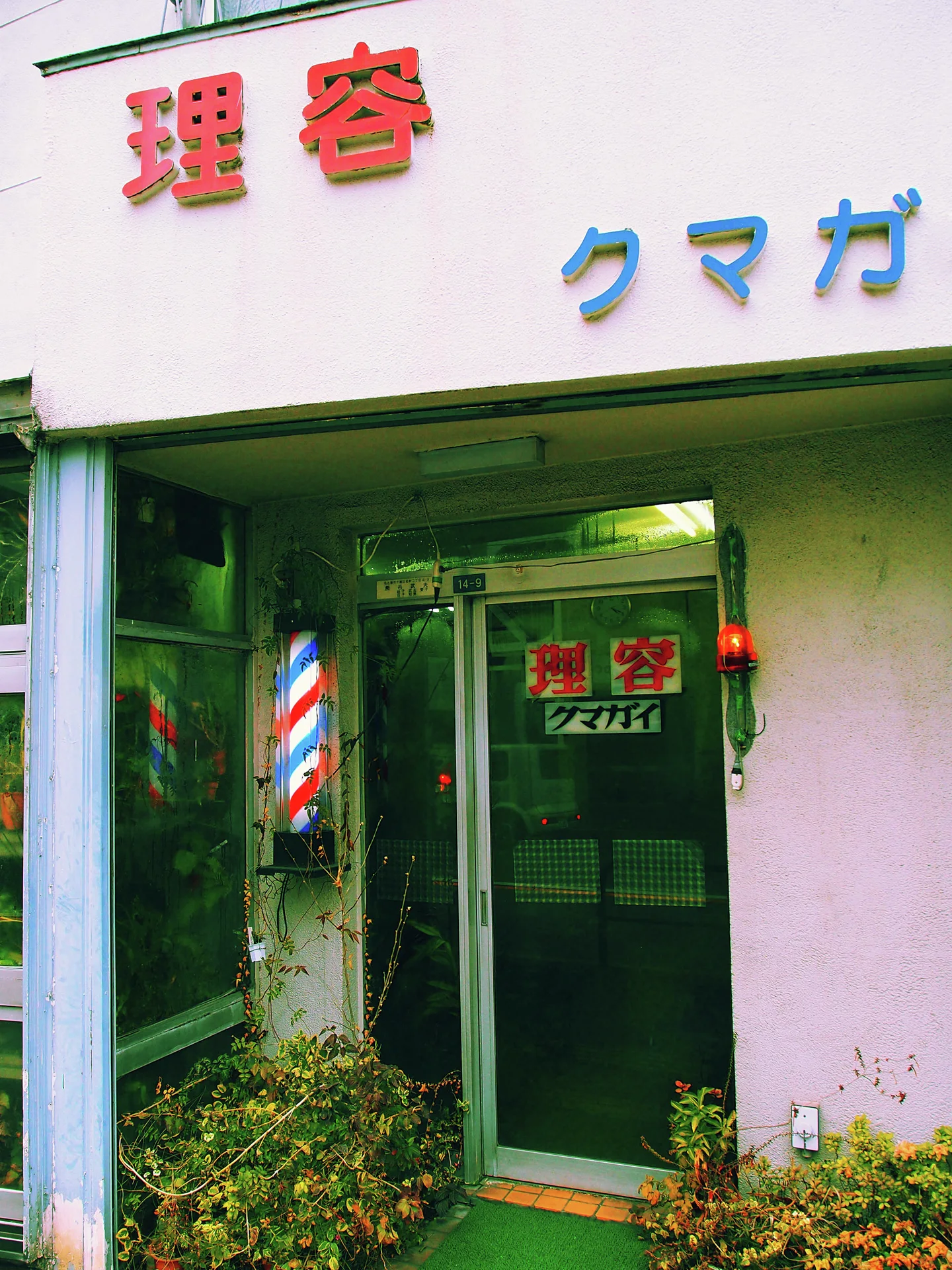 A striped barber pole stands beside a glass door beneath raised red and blue characters.