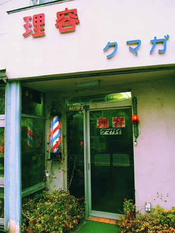 A striped barber pole stands beside a glass door beneath raised red and blue characters.