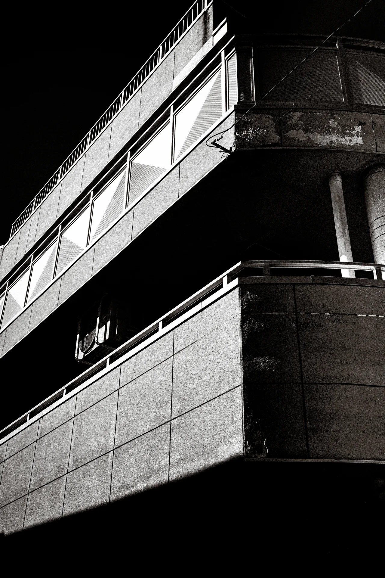 Sunlight strikes concrete balcony edges while deep shadows conceal the building's interior in black and white.