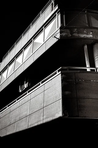 Sunlight strikes concrete balcony edges while deep shadows conceal the building's interior in black and white.