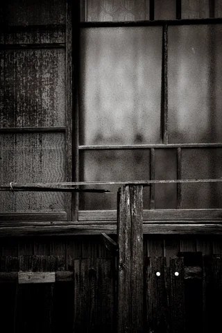 Weathered wooden framing surrounds cloudy window panes and a vertical post in black and white.